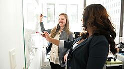 Zwei Frauen arbeiten an einem Whiteboard.