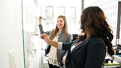 Zwei Frauen arbeiten an einem Whiteboard.
