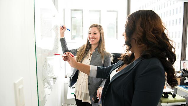 Zwei Frauen arbeiten an einem Whiteboard.