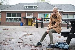 Ein junges Mädchen sitzt auf einer Bank auf dem Schulhof und schaut betreten zu Boden.