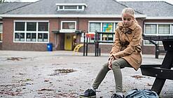 Ein junges Mädchen sitzt auf einer Bank auf dem Schulhof und schaut betreten zu Boden.