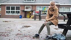 Ein junges Mädchen sitzt auf einer Bank auf dem Schulhof und schaut betreten zu Boden.