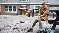 Ein junges Mädchen sitzt auf einer Bank auf dem Schulhof und schaut betreten zu Boden.