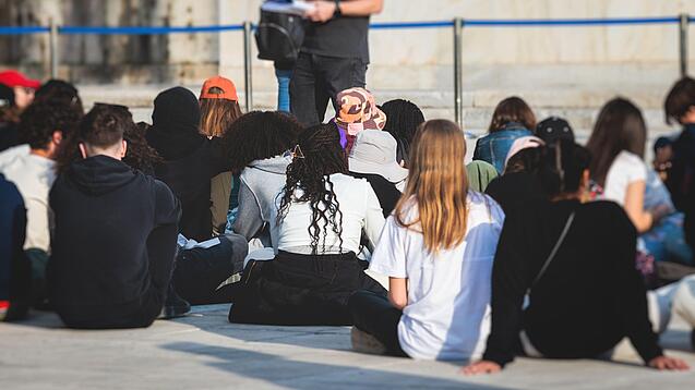Gruppe junger Menschen sitzt auf dem Boden und hört sich einen Vortrag an