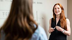 Eine junge Lehrerein steht an einem Whiteboard.