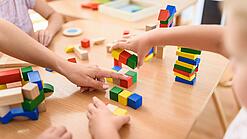 Mehrere Kinder spielen auf einem Tisch mit verschiedenfarbenen Holzklötzchen.