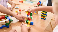 Mehrere Kinder spielen auf einem Tisch mit verschiedenfarbenen Holzklötzchen.