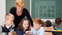 Lehrerin und Grundschüler:innen in einem Klassenraum.