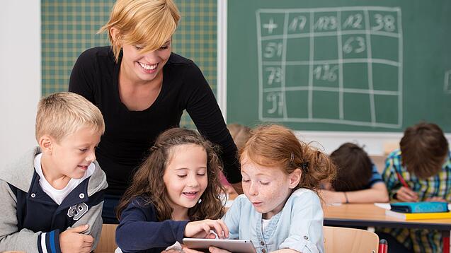 Lehrerin und Grundschüler:innen in einem Klassenraum.