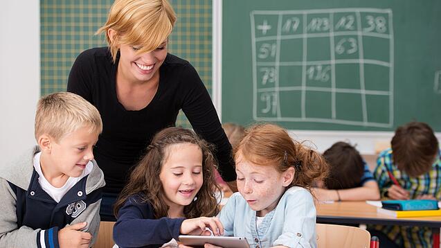 Lehrerin und Grundschüler:innen in einem Klassenraum.