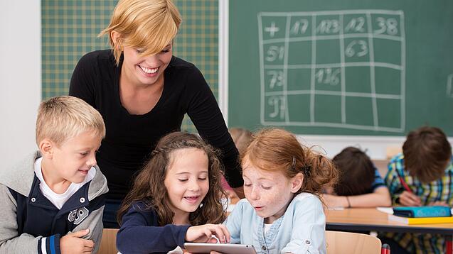Lehrerin und Grundschüler:innen in einem Klassenraum.