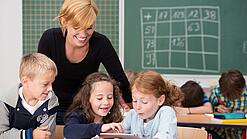 Lehrerin und Grundschüler:innen in einem Klassenraum.