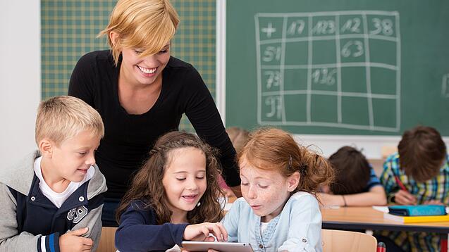 Lehrerin und Grundschüler:innen in einem Klassenraum.