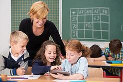 Lehrerin und Grundschüler:innen in einem Klassenraum.
