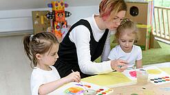 Eine Erzieherin bastelt mit zwei Kindern in einer Kita.