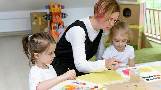 Eine Erzieherin bastelt mit zwei Kindern in einer Kita.