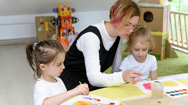Eine Erzieherin bastelt mit zwei Kindern in einer Kita.