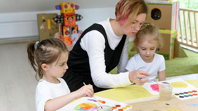 Eine Erzieherin bastelt mit zwei Kindern in einer Kita.