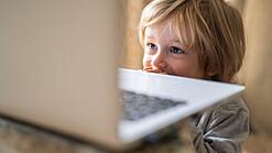 Ein kleiner junge steht vor einem Laptop und schaut auf den Bildschirm.