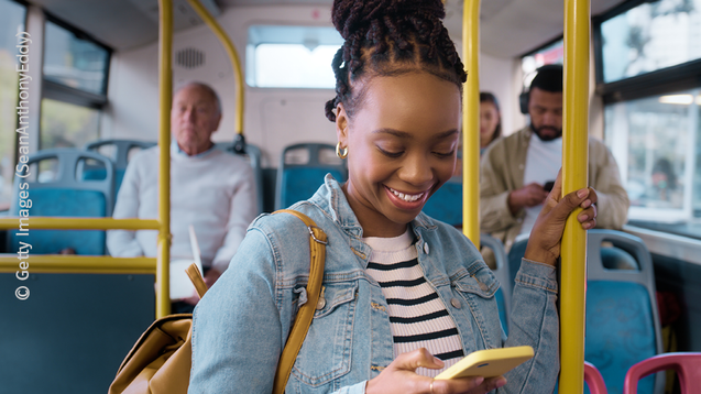 Junge Frau steht in einem Bus und schaut auf ihr Smartphone.