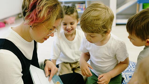 Eine Erzieherin liest Kindern im Kindergartenalter ein Buch vor.