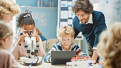 Schüler:innen tragen Schutzbrillen und arbeiten mit einem Mikroskop. 