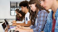 Jugendliche sitzen in der Schule an Laptops.