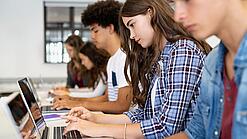 Jugendliche sitzen in der Schule an Laptops.