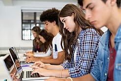 Jugendliche sitzen in der Schule an Laptops.