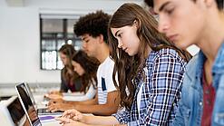 Jugendliche sitzen in der Schule an Laptops.