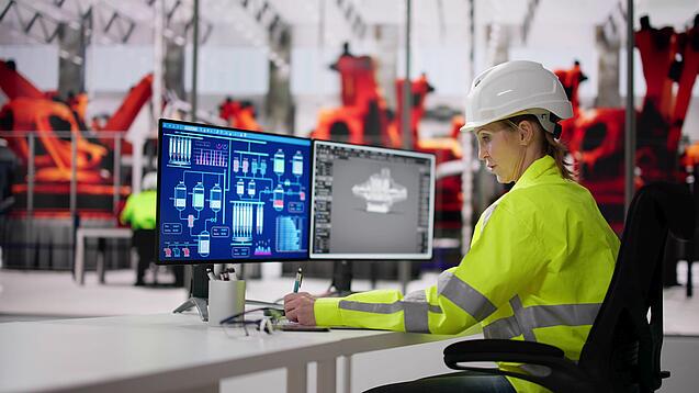 Frau in Warnweste sitzt an einem Computer und überprüft technische Daten.