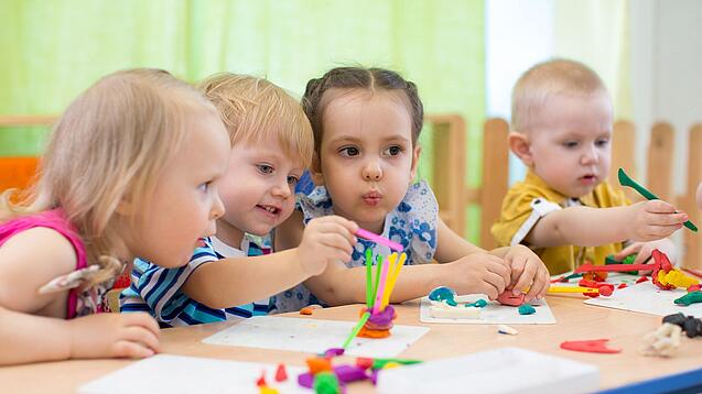 Kleinkinder sitzen an einem Tisch und spielen.