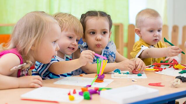 Kleinkinder sitzen an einem Tisch und spielen.
