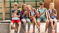 Kinder sitzen auf einer Bank auf dem Schulhof und schauen auf ihre Handys.