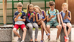 Kinder sitzen auf einer Bank auf dem Schulhof und schauen auf ihre Handys.