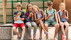 Kinder sitzen auf einer Bank auf dem Schulhof und schauen auf ihre Handys.