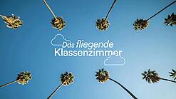 "Das fliegende Klassenzimmer" steht in weißer Schrift auf dem blauen Himmel, umrandet von Palmen.