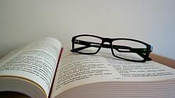 Eine Brille liegt auf einem aufgeschlagenen Buch.