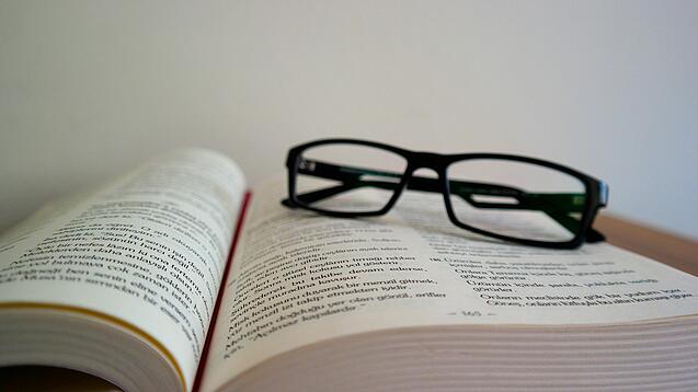 Eine Brille liegt auf einem aufgeschlagenen Buch.