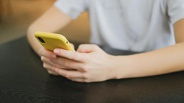 Hände halten ein Smartphone in einer gelben Hülle.