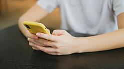 Hände halten ein Smartphone in einer gelben Hülle.