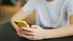 Hände halten ein Smartphone in einer gelben Hülle.