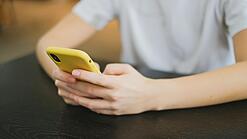 Hände halten ein Smartphone in einer gelben Hülle.