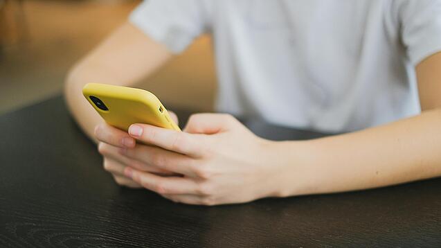 Hände halten ein Smartphone in einer gelben Hülle.