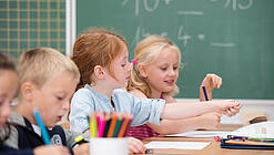 Kinder sitzen in der Grundschule an einem Tisch und lernen Mathematik.
