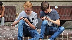 Zwei Jungs sitzen auf dem Schulhof und spielen auf ihren Smartphones.