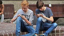 Zwei Jungs sitzen auf dem Schulhof und spielen auf ihren Smartphones.