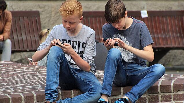 Zwei Jungs sitzen auf dem Schulhof und spielen auf ihren Smartphones.