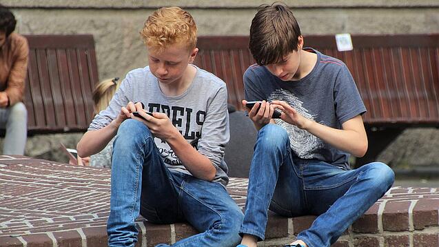 Zwei Jungs sitzen auf dem Schulhof und spielen auf ihren Smartphones.