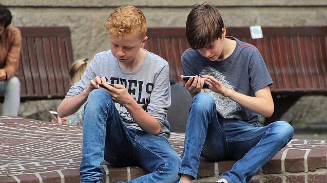 Zwei Jungs sitzen auf dem Schulhof und spielen auf ihren Smartphones.